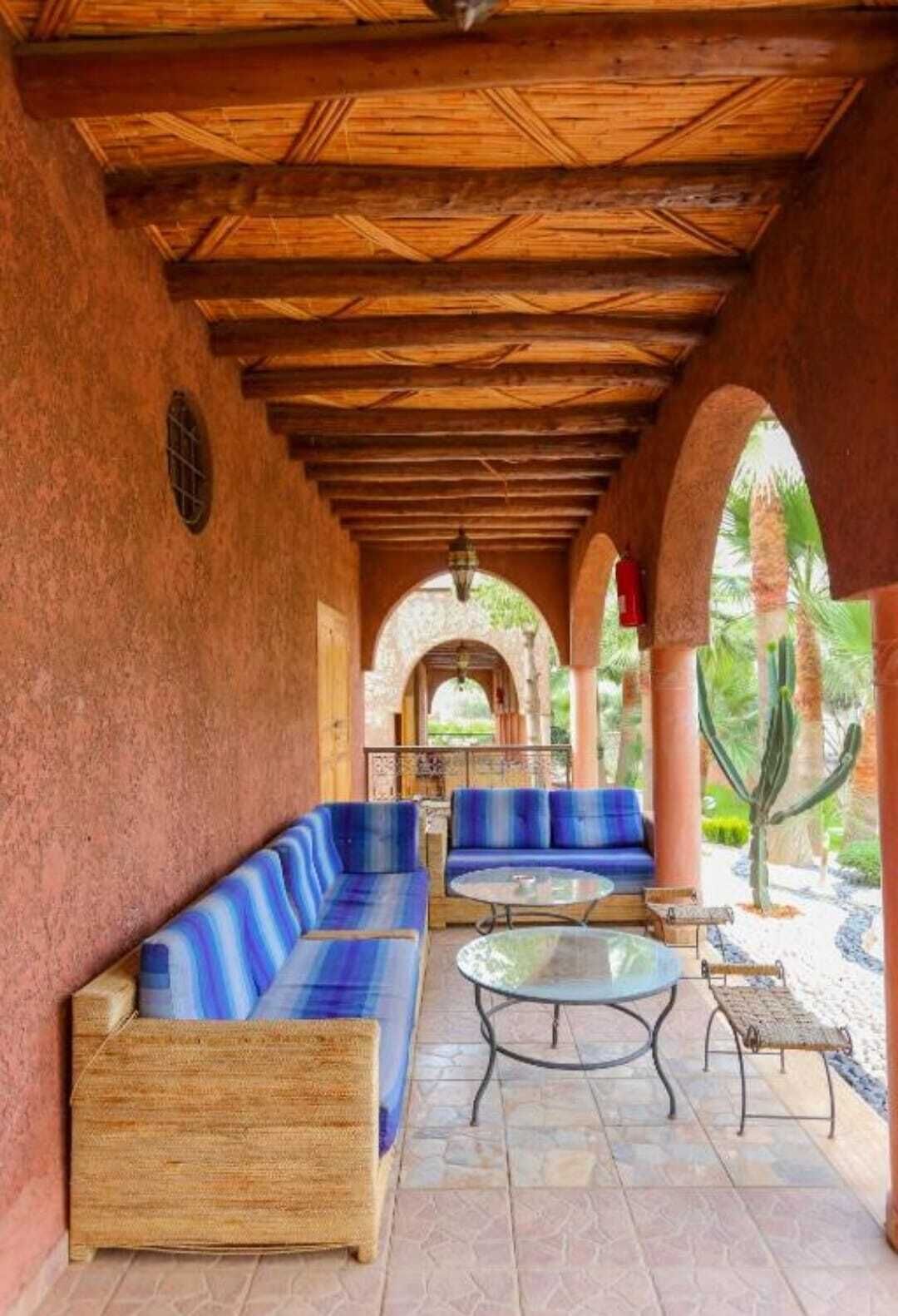 Un área con mesas y bancos de madera, rodeada de arcos y vistas a palmeras.