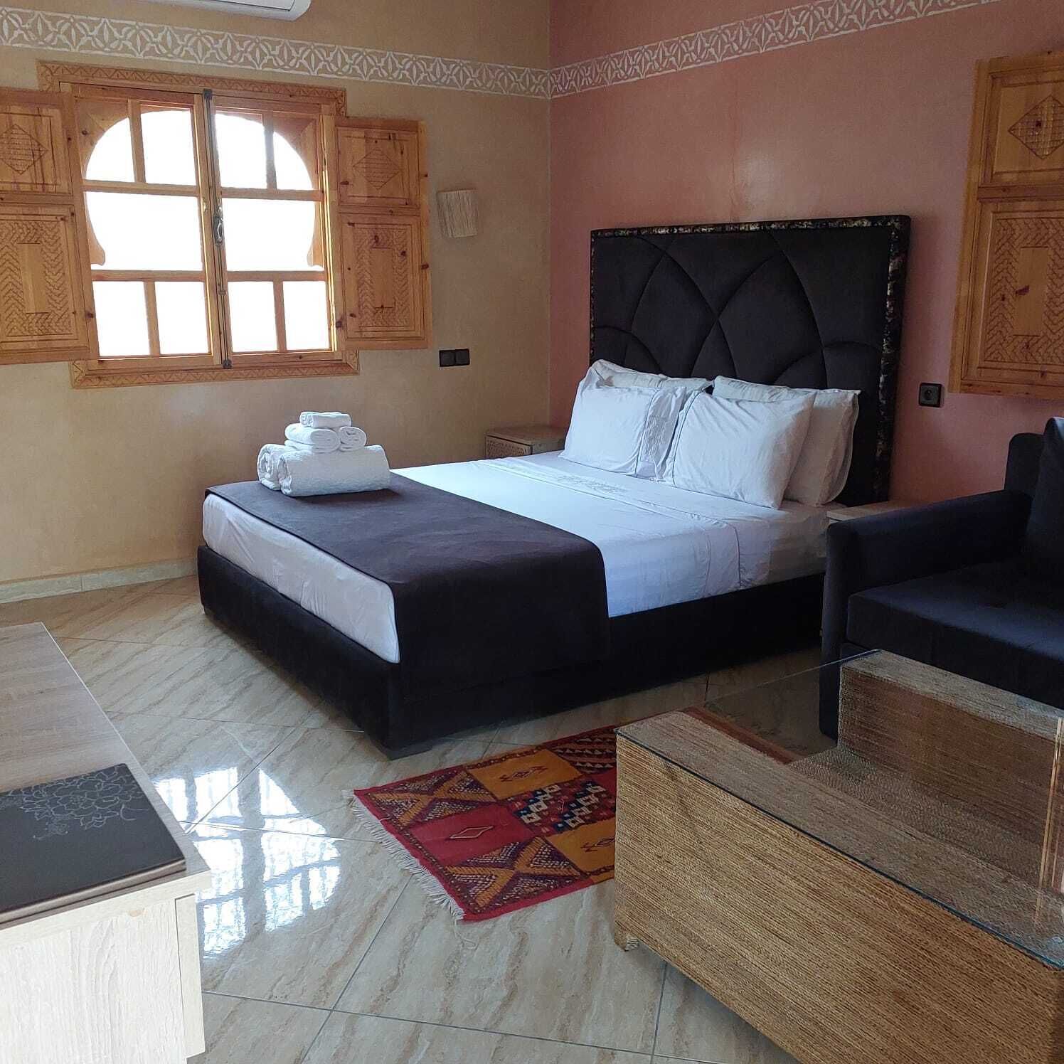 A bedroom with a bed, a chair, a small table, and a window.