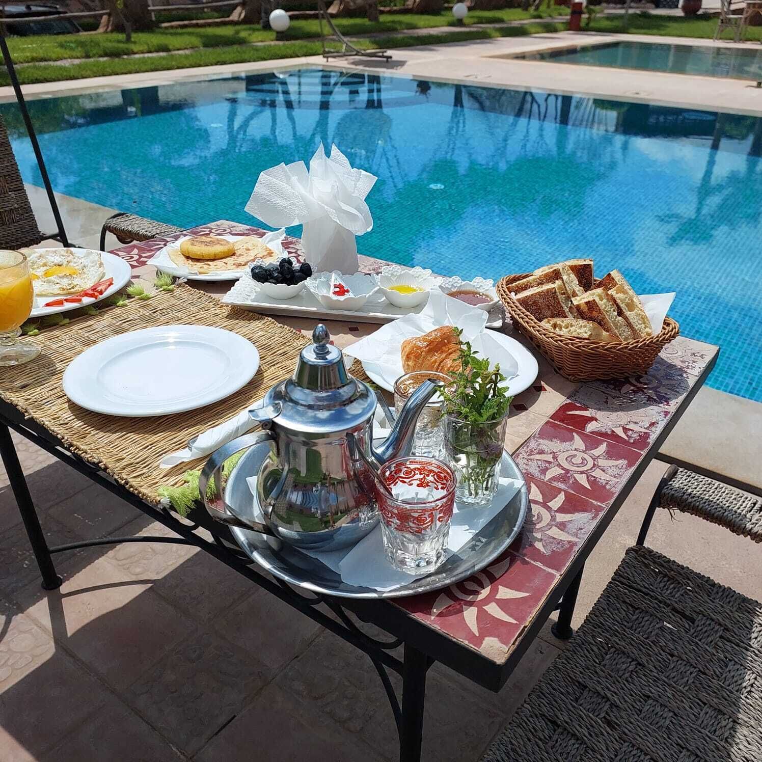 Ein Frühstückstisch am Pool mit Speisen, einem Teekessel und Gläsern.