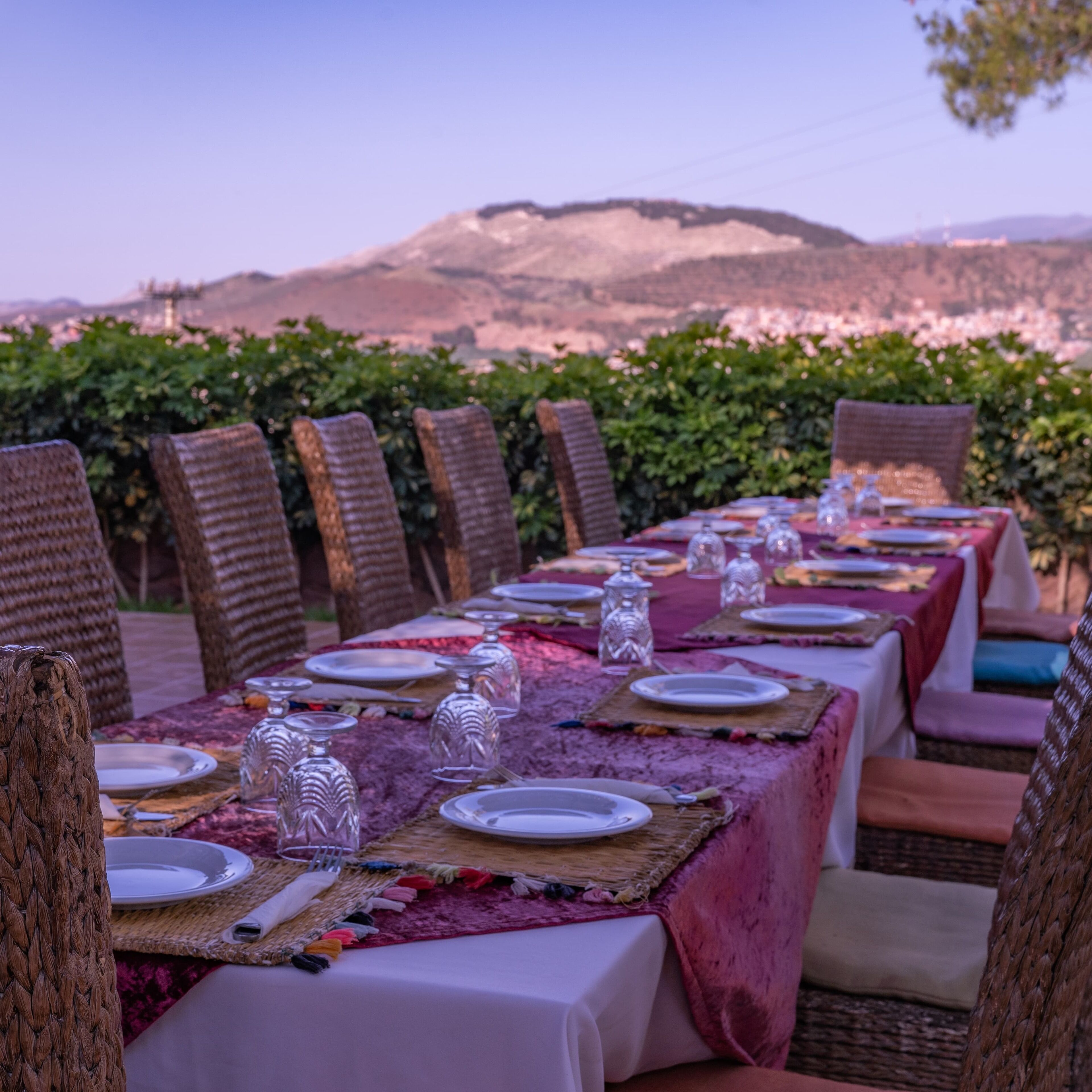 A long dining table set outdoors with chairs, plates, and glassware.