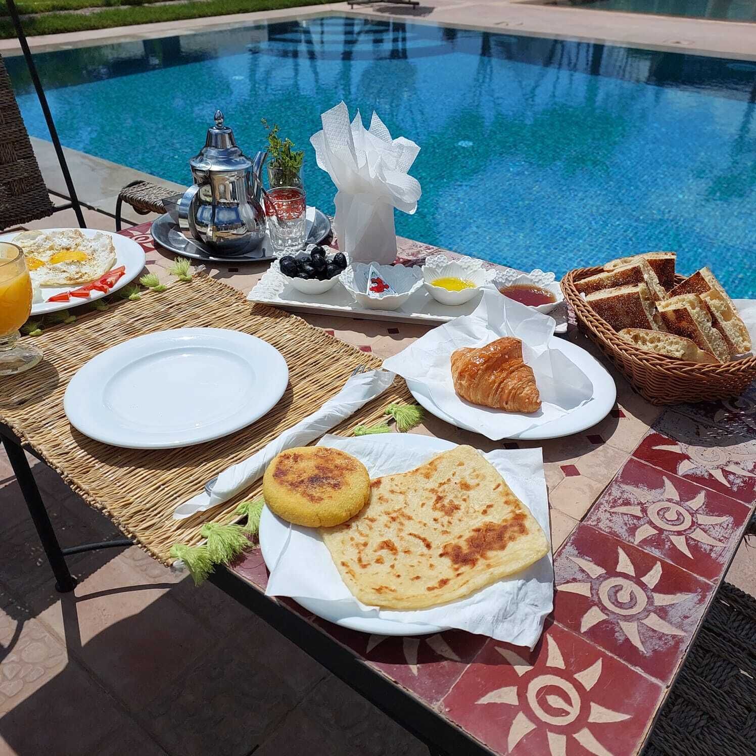 A breakfast setup by a pool with plates, toast, croissants, and a beverage.