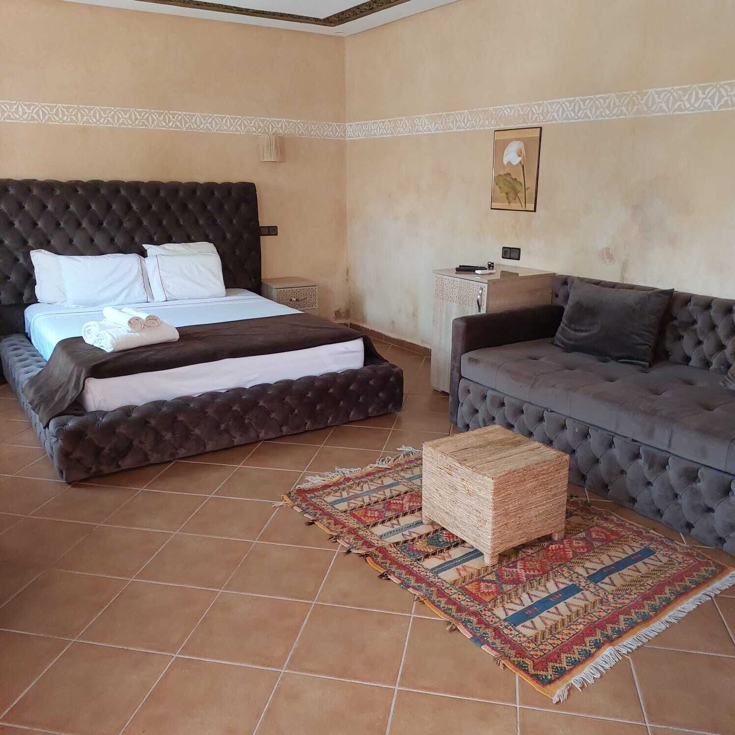 A bedroom with a large bed, a grey sofa, a small table, and a patterned rug.