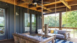 A wooden deck with a swing, a cushioned bench, and a table with a laptop.