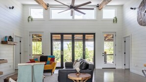 A spacious living area with a high ceiling, large windows, and a ceiling fan.