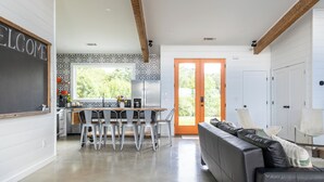 A modern kitchen with a dining area, a black leather sofa, and a 'WELCOME' sign on the wall.