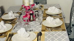 Une table à manger dressée avec de l’argenterie blanche, des verres et des couverts, agrémentée de fleurs roses et de bougies.