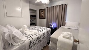 Une chambre d’hôtel avec deux lits, un ventilateur de plafond, une table de chevet avec une lampe, une armoire et un tableau encadré au mur.