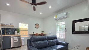 A modern living room with a leather sofa, a ceiling fan, and a kitchen area with a dishwasher and a sink.