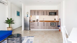 Una cocina moderna con armarios de madera, un microondas y un horno empotrado. Hay un sofá azul y una pequeña mesa con una planta.