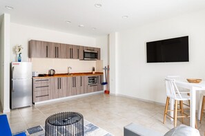 A modern kitchen with wooden cabinets, a built-in microwave, and a dining area with white chairs and a table. - Bushiri's Long Life Building-2BD/1BA APT-Sleeps 4 (Oranjestad)