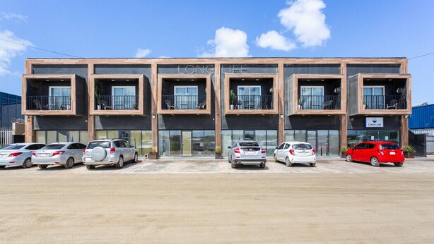 Un edificio moderno con techo plano, varios balcones y un estacionamiento con varios coches.