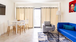 Una sala de estar moderna con un sofá azul, un sillón gris, una mesa de comedor con sillas y una mesa de centro.