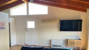 Een woonkamer met een zwarte bank, een aan de muur bevestigde televisie en een raam dat voor natuurlijk licht zorgt.