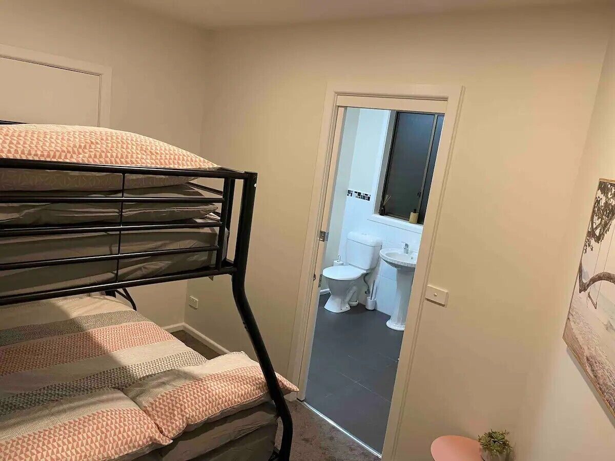 Un lit superposé dans une chambre avec une porte donnant sur une salle de bain équipée de toilettes et d’un lavabo.