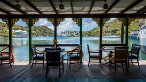 A covered outdoor seating area with wooden furniture and a view of the water and mountains. - Villa in marigot bay. Breakfast inclusive. 2 mins walk to the beach (Castries)