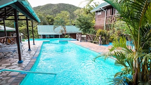 A rectangular swimming pool with a tiled deck, surrounded by wooden structures and lush greenery. - Villa in marigot bay. Breakfast inclusive. 2 mins walk to the beach (Castries)