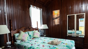 A wooden-paneled room with a bed, two bedside tables, a mirror, and a window with curtains. - Villa in marigot bay. Breakfast inclusive. 2 mins walk to the beach (Castries)