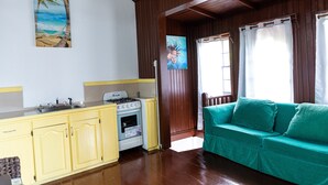 A kitchen with yellow cabinets, a stove, and a sink. There is a green sofa and a painting of a beach scene. - Villa in marigot bay. Breakfast inclusive. 2 mins walk to the beach (Castries)