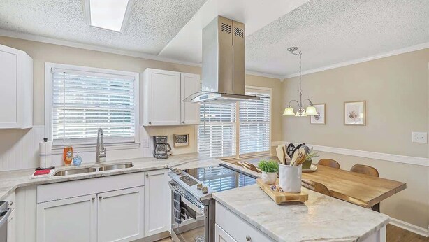 A modern kitchen with white cabinets, a built-in oven, a stainless steel range, and a wooden dining table with chairs. - Family Fun near CHAS Summerville and Nexton (Summerville)