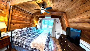Een gezellige slaapkamer in een chalet, met een bed, plafondventilator, televisie en een raam met gordijnen.