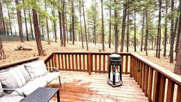Una terraza de madera con una parrilla, un banco y vistas a un bosque.