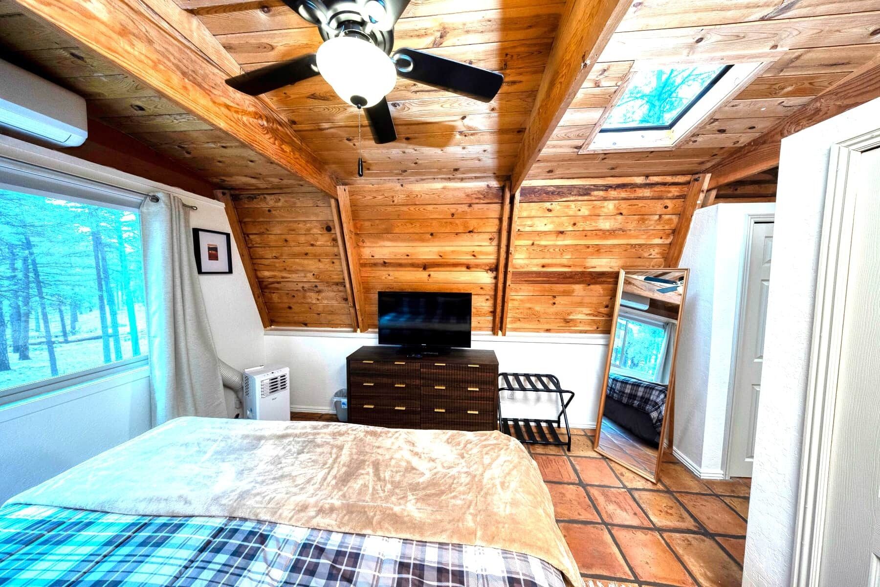 A bedroom with a bed, a television, a dresser, and a ceiling fan.