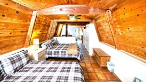 A cabin with a sloped ceiling, wooden walls, a bed with plaid bedding, a nightstand, a dresser, and a ceiling fan. - Grand Gateway Cabin | 1-Acre Pine Retreat, Rt. 66 (Williams)