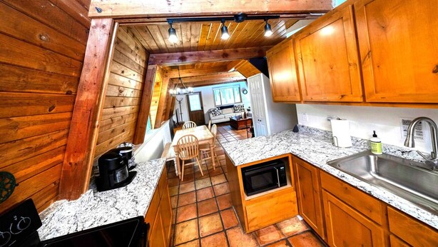 A compact kitchen with wooden cabinets, a granite countertop, and a built-in microwave. - Grand Gateway Cabin | 1-Acre Pine Retreat, Rt. 66 (Williams)