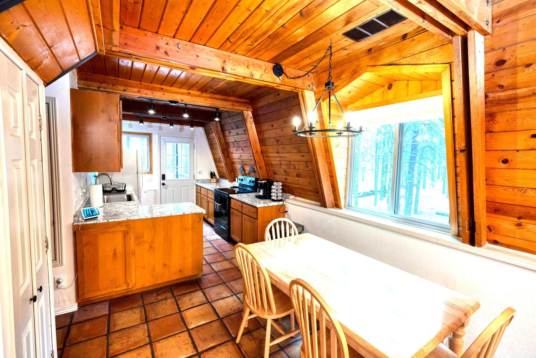 Interior acogedor de una cabaña con cocina, comedor y ventana con vistas a árboles.