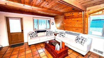Interior acogedor de una cabaña con techo de madera, un conjunto de sofás, una mesa de centro y un ventanal con vistas a un paisaje nevado.