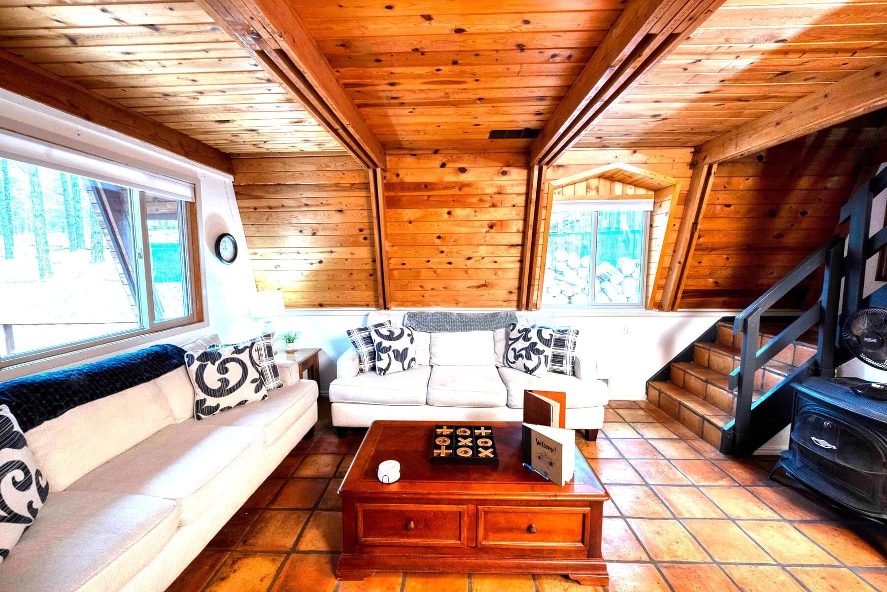 A wooden cabin interior with a sofa, a coffee table, and a staircase.
