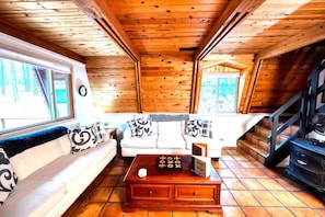 A wooden cabin interior with a sofa, a coffee table, and a staircase. - Grand Gateway Cabin | 1-Acre Pine Retreat, Rt. 66 (Williams)