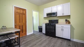 Une cuisine avec une table en bois, des placards blancs, une cuisinière et un four à micro-ondes.