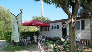 Een rij fietsen geparkeerd voor een gebouw, met een rode parasol, een bord en een boom.