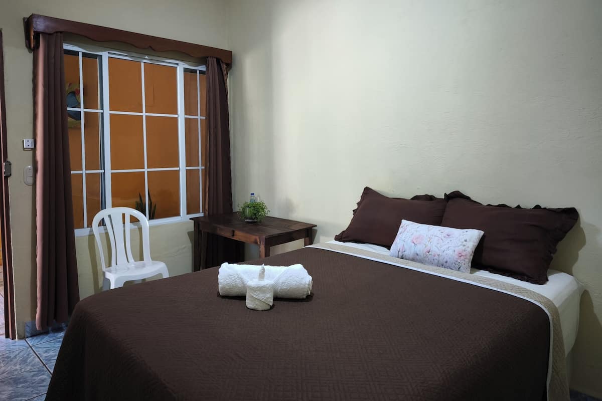 Une chambre d’hôtel avec un lit, une petite table, une chaise et une fenêtre avec des rideaux.