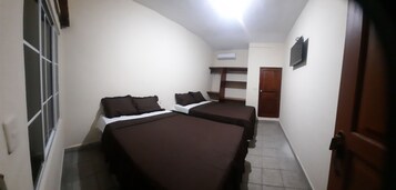 Una habitación pequeña y tenuemente iluminada con dos camas, una puerta de madera y una ventana con barrotes.
