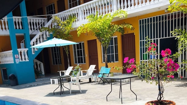 A swimming pool with lounge chairs and a table, surrounded by a building with balconies and potted plants. - Hotel y Restaurante Casa Jardines (San Benito)