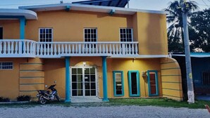 A two-story building with a balcony, a motorcycle parked in front, and a sign advertising apartments, offices, and local services. - Hotel y Restaurante Casa Jardines (San Benito)