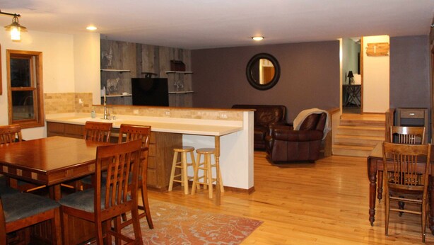 A spacious living area with a wooden dining table, kitchen island, and a cozy seating area with a leather couch. - Brigham View (Barneveld)
