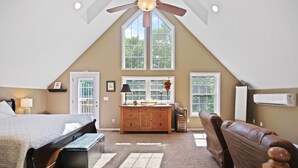 A bedroom with a sloped ceiling, a bed, a dresser, a vanity, a window, and a ceiling fan.