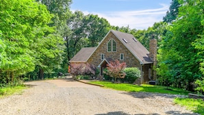 A stone house with a gravel driveway, surrounded by lush greenery.