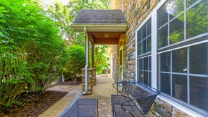 A covered patio with outdoor seating, stone walls, and a view of a stone building.