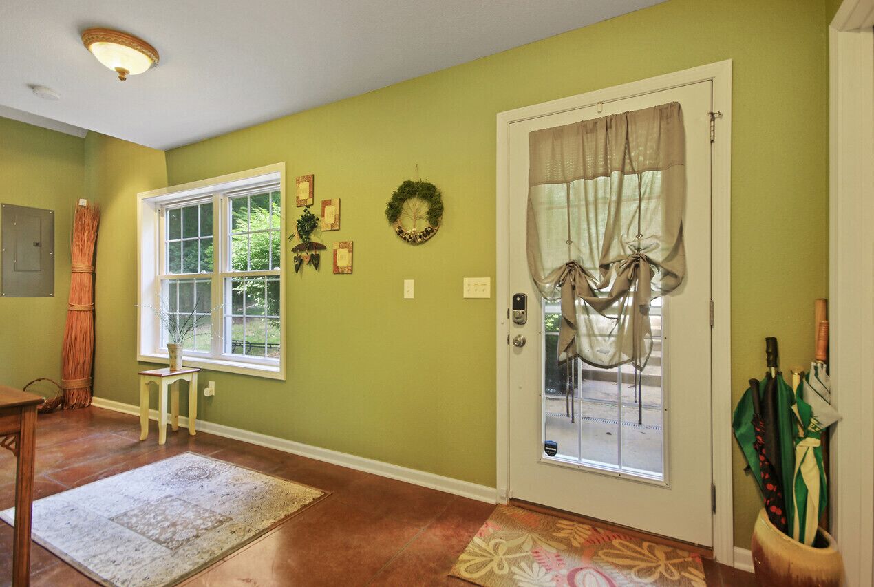 A hallway with a wooden floor, a door with a glass panel, a small table with a vase, and a wreath on the wall.