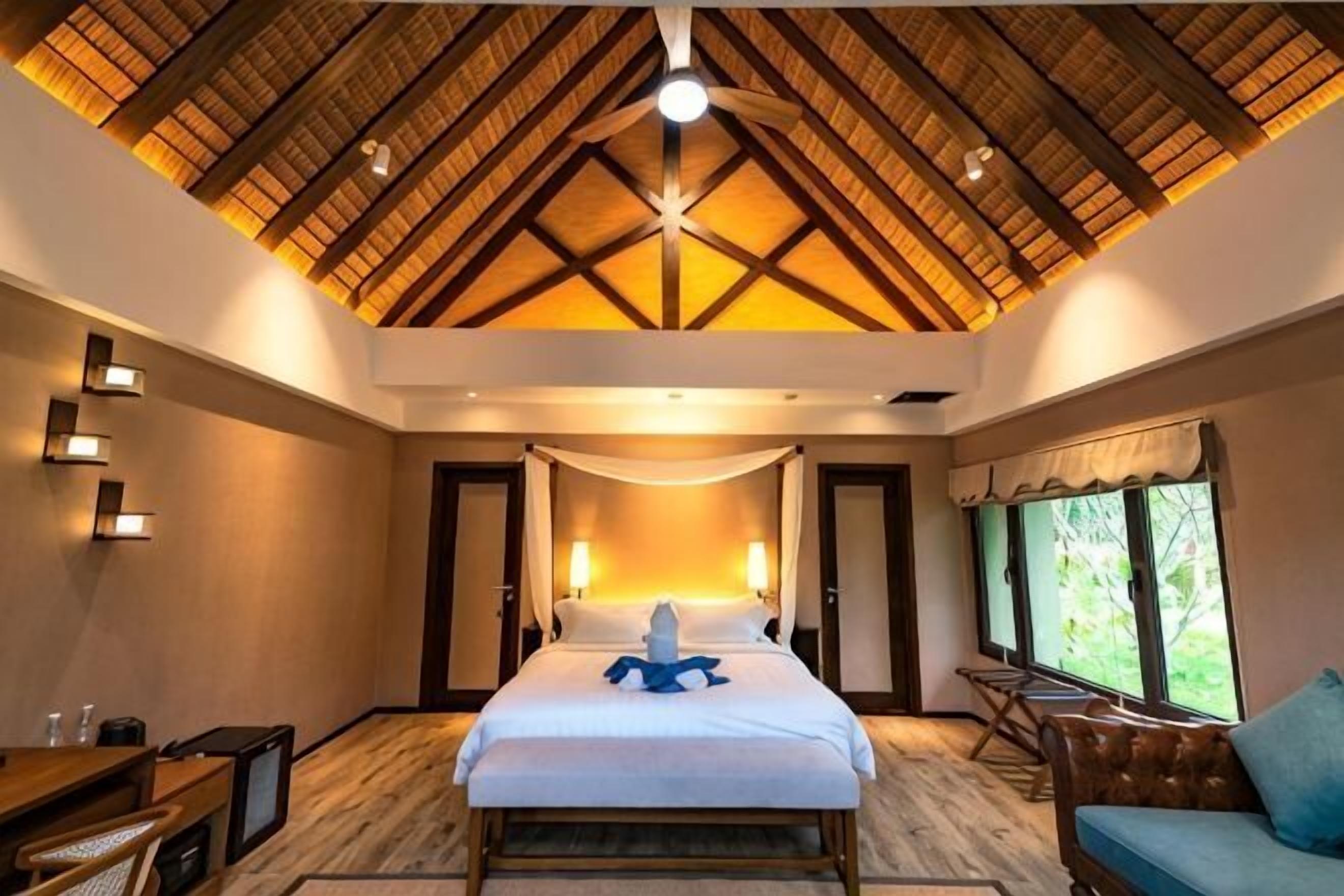 A bedroom with a high ceiling, a bed, a desk, and a chair.