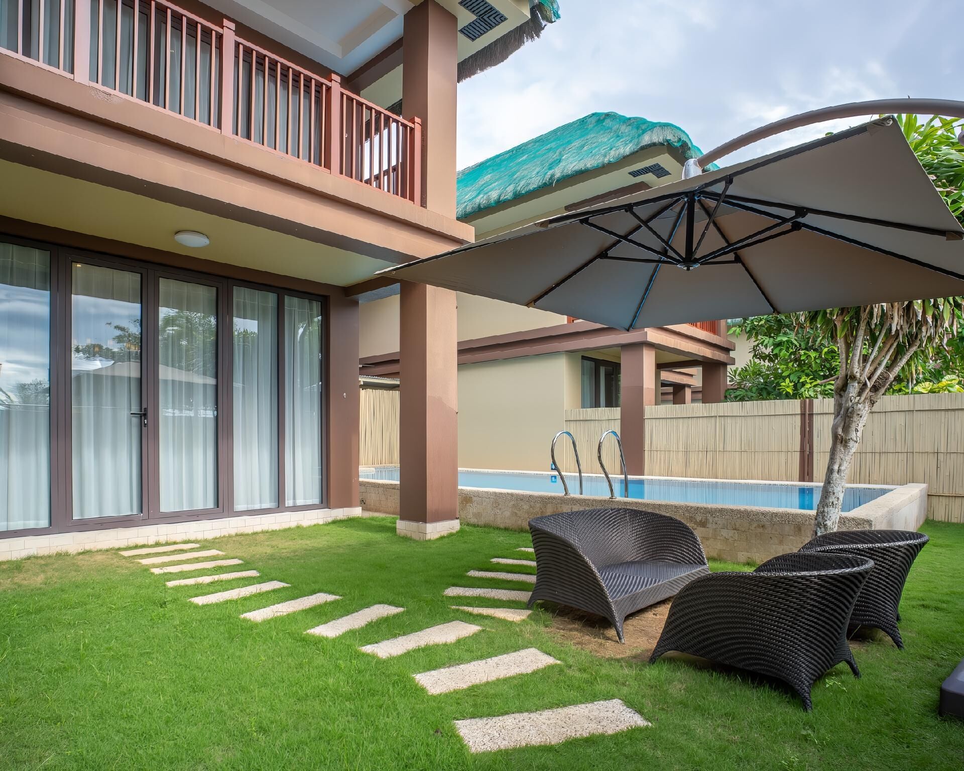 Un patio con piscina, mobiliario exterior y un área techada con sombrilla.