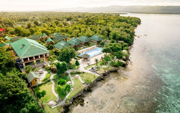 Vista aérea de un complejo turístico con varias edificaciones, una piscina y una playa.