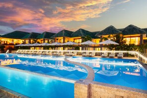 A pool area with lounge chairs and umbrellas, surrounded by buildings with thatched roofs. - H Resort Bohol - The Coral Cliff by SMS Hospitality (Calape)