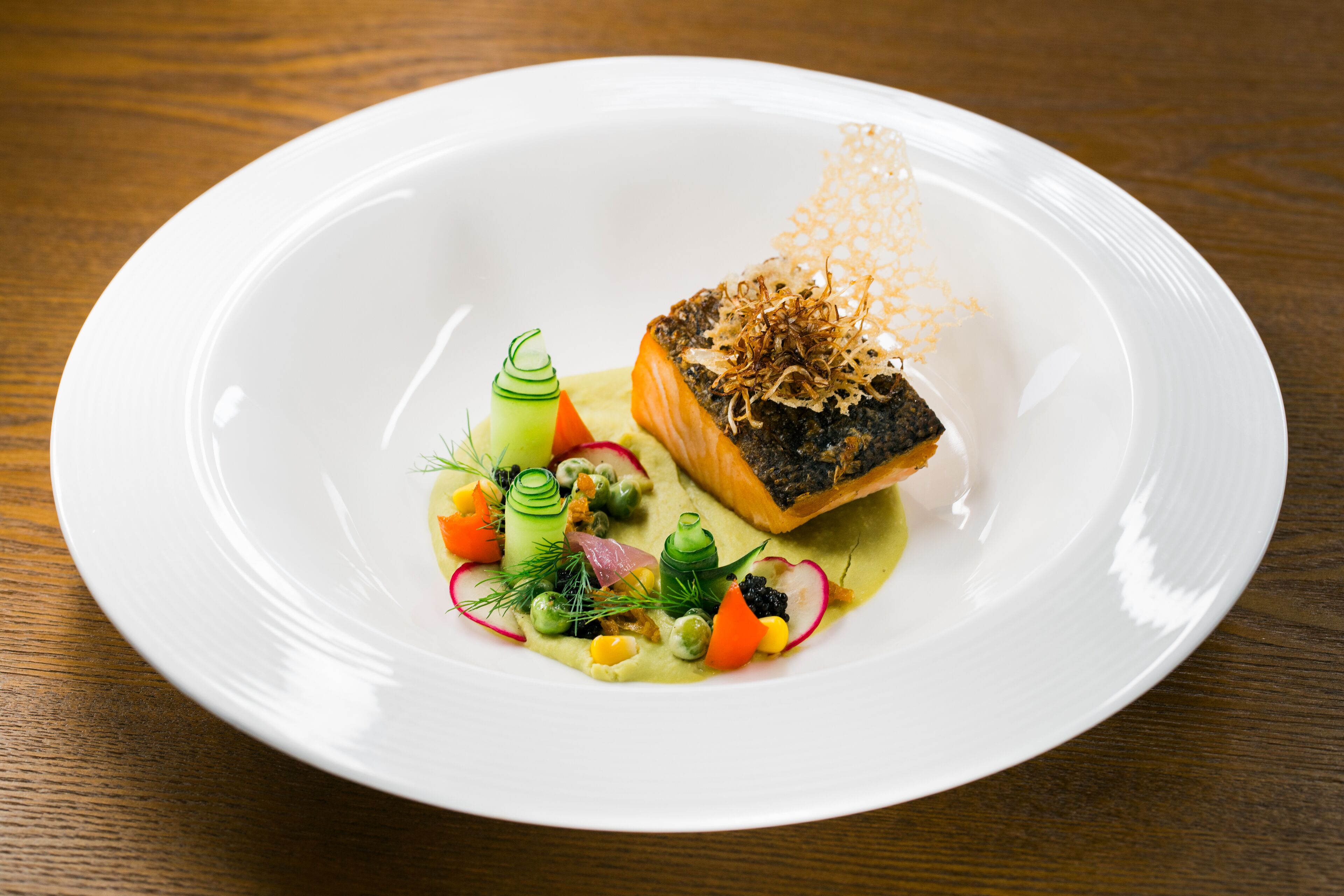A white plate with a piece of salmon, garnished with dill and microgreens, on a wooden table.