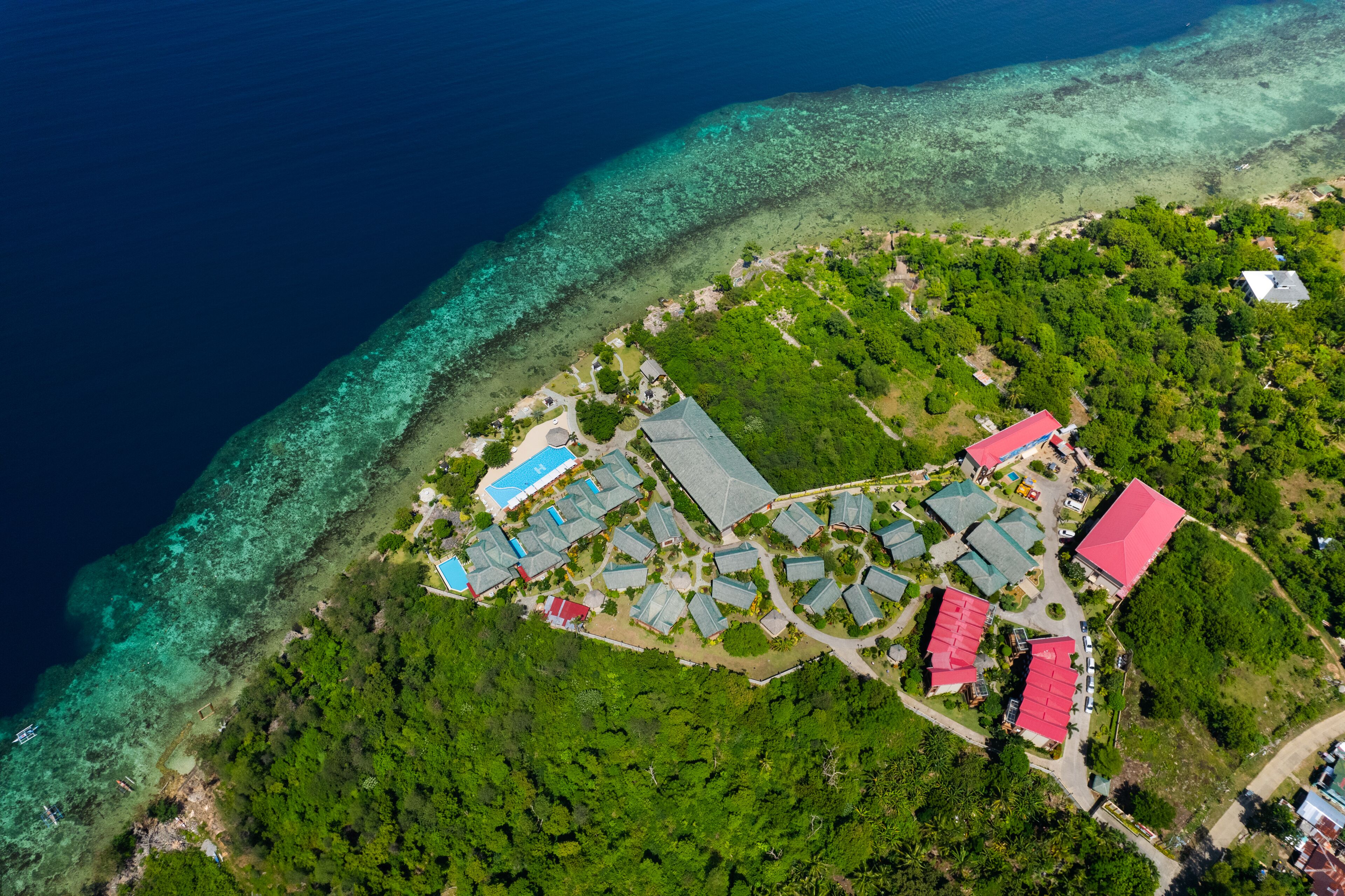 Une vue aérienne d’un complexe hôtelier comprenant plusieurs bâtiments, une mer d’un bleu limpide et un paysage verdoyant luxuriant.