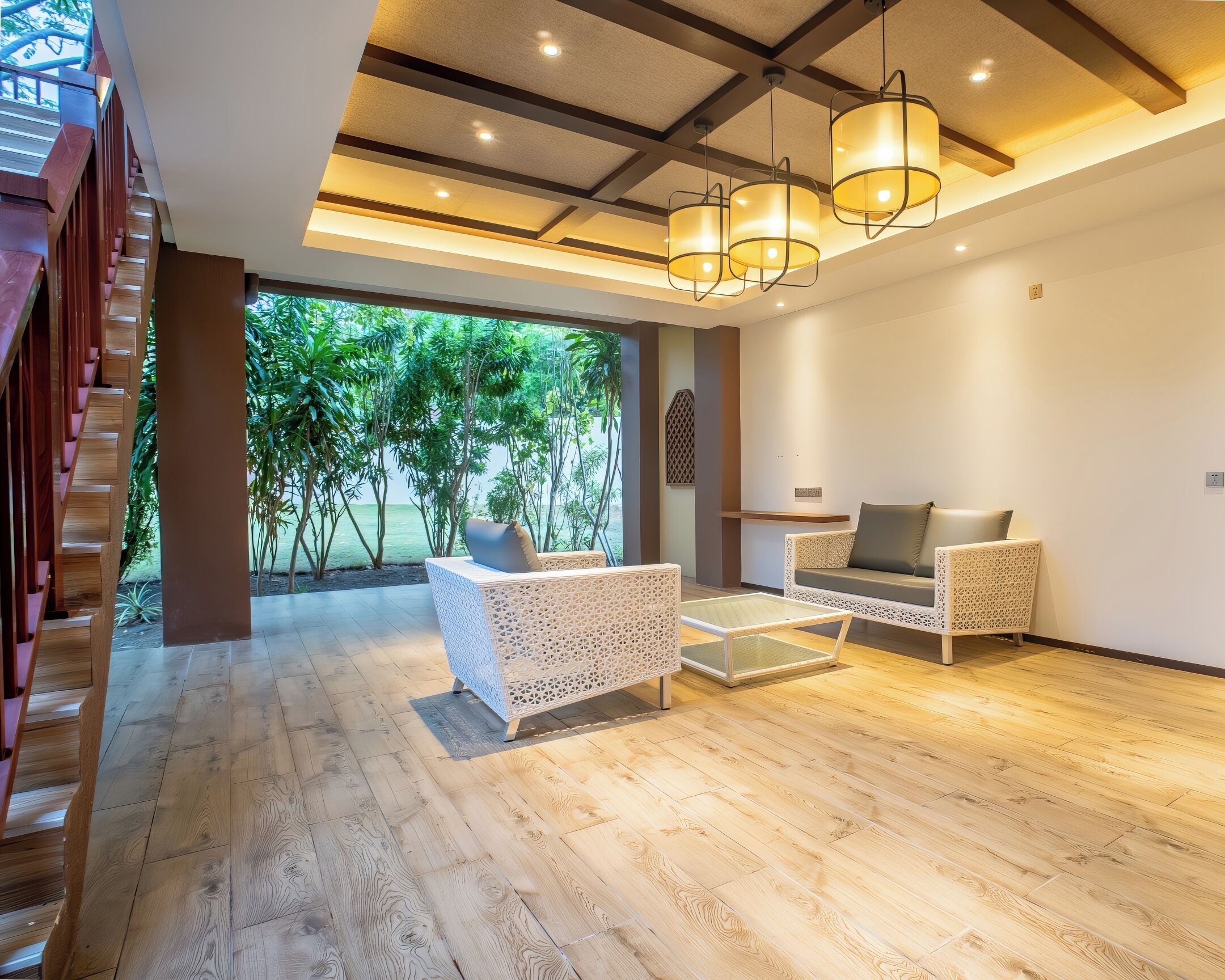 A spacious living area with a wooden floor, two white wicker sofas, a glass coffee table, and a staircase with wooden railings.
